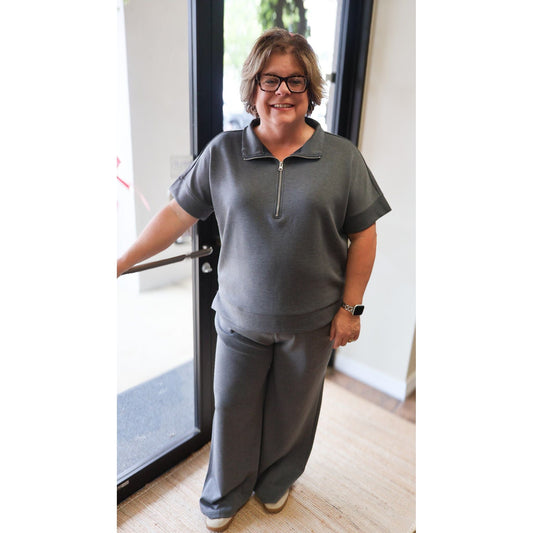 A woman wearing an Annie Ks Boutique charcoal scuba knit half-zip top and matching wide-leg pants set.