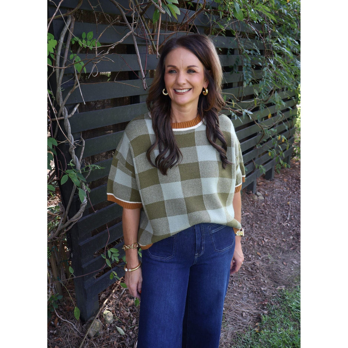 Annie Ks Boutique model wearing a sage and olive checkered drop shoulder sweater with dark wash jeans outdoors