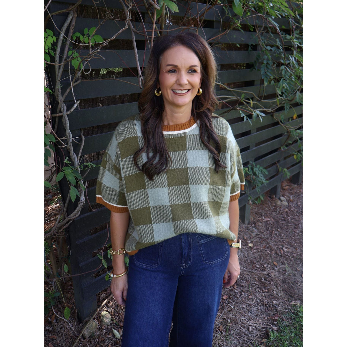 Annie Ks Boutique model wearing a sage and olive checkered plush knit sweater with drop shoulders and dark denim jeans