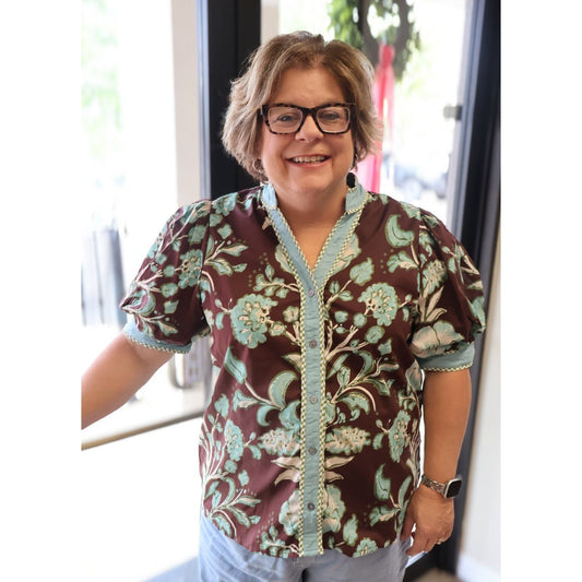 A woman wearing an Annie Ks Boutique chocolate brown floral puff sleeve top with light blue contrast trim and buttons.