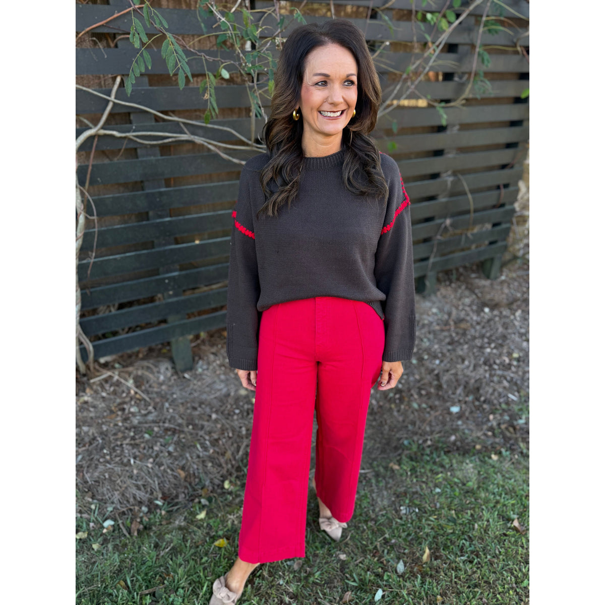Annie Ks Boutique chocolate brown sweater with red blanket-stitch detail worn by a woman with bright red trousers.