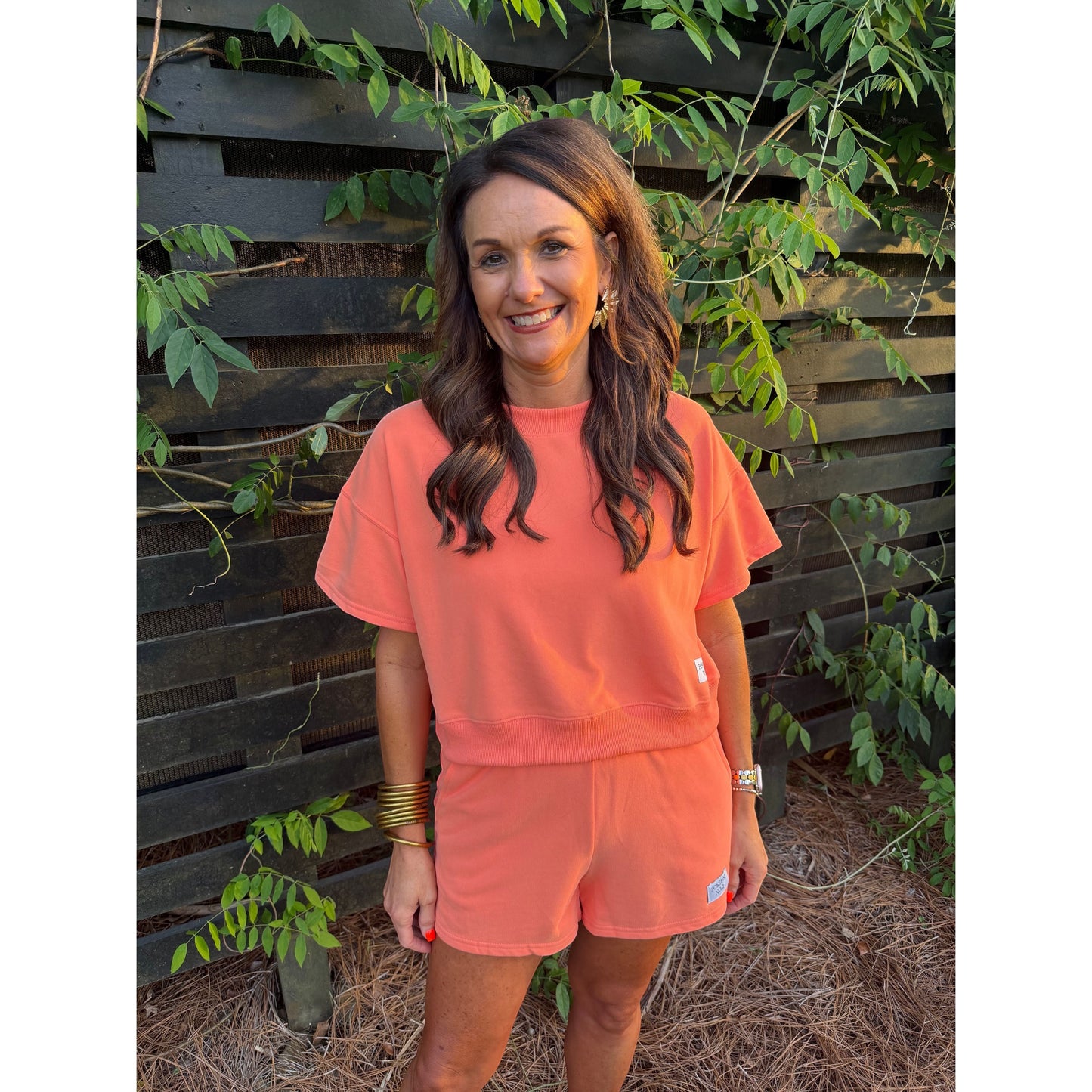 Annie Ks Boutique Watermelon Sugar coral cotton blend short set worn by a woman outdoors against a wooden fence.