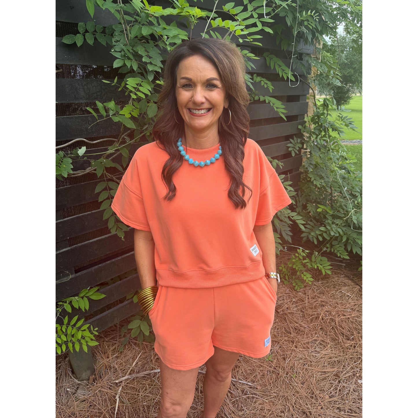 Annie Ks Boutique Watermelon Sugar coral cotton blend short set worn by a smiling woman with a turquoise necklace.