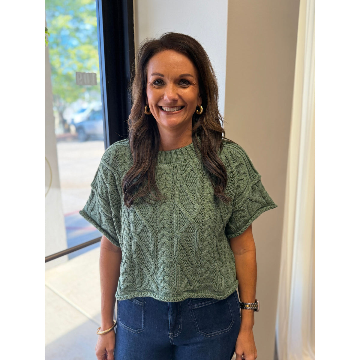 Annie Ks Boutique dusty green cropped knit sweater with a round neck and cable knit texture worn by a smiling woman