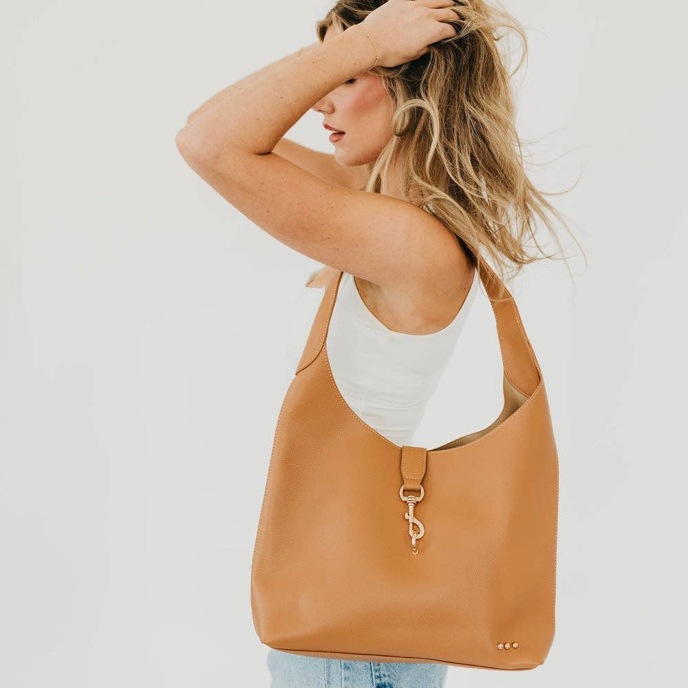 Annie Ks Boutique Haddie Hobo brown vegan leather tote bag with gold lock accent worn over the shoulder by a woman