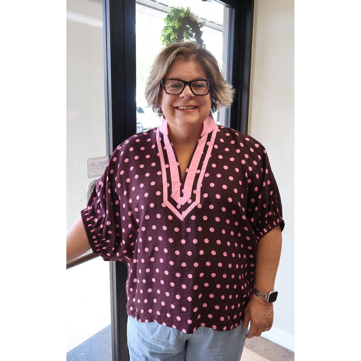 Annie Ks Boutique curvy merlot polka dot dolman top with a pink contrast V-neck collar worn by a smiling woman