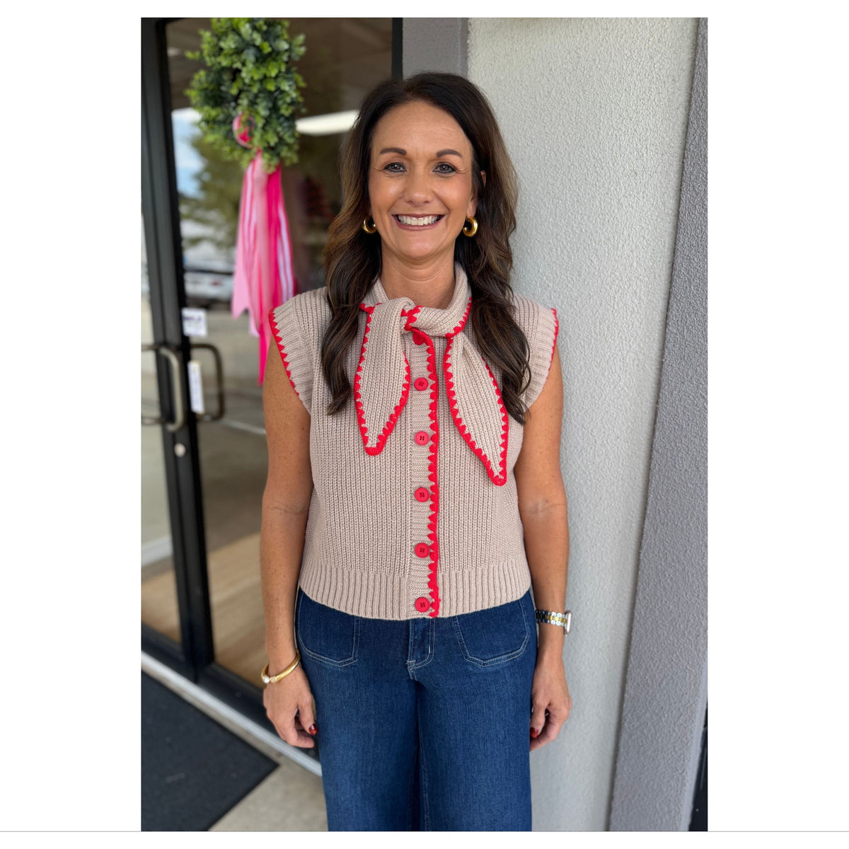 Annie Ks Boutique mocha sweater vest with red contrast stitching, tie neck, and button front worn by a smiling woman