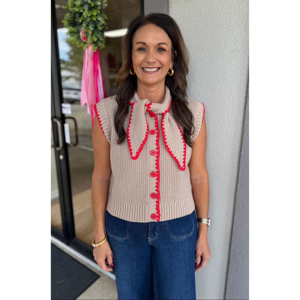 Annie Ks Boutique mocha sweater vest with red blanket stitching, tie neck, and button front worn by a smiling woman.