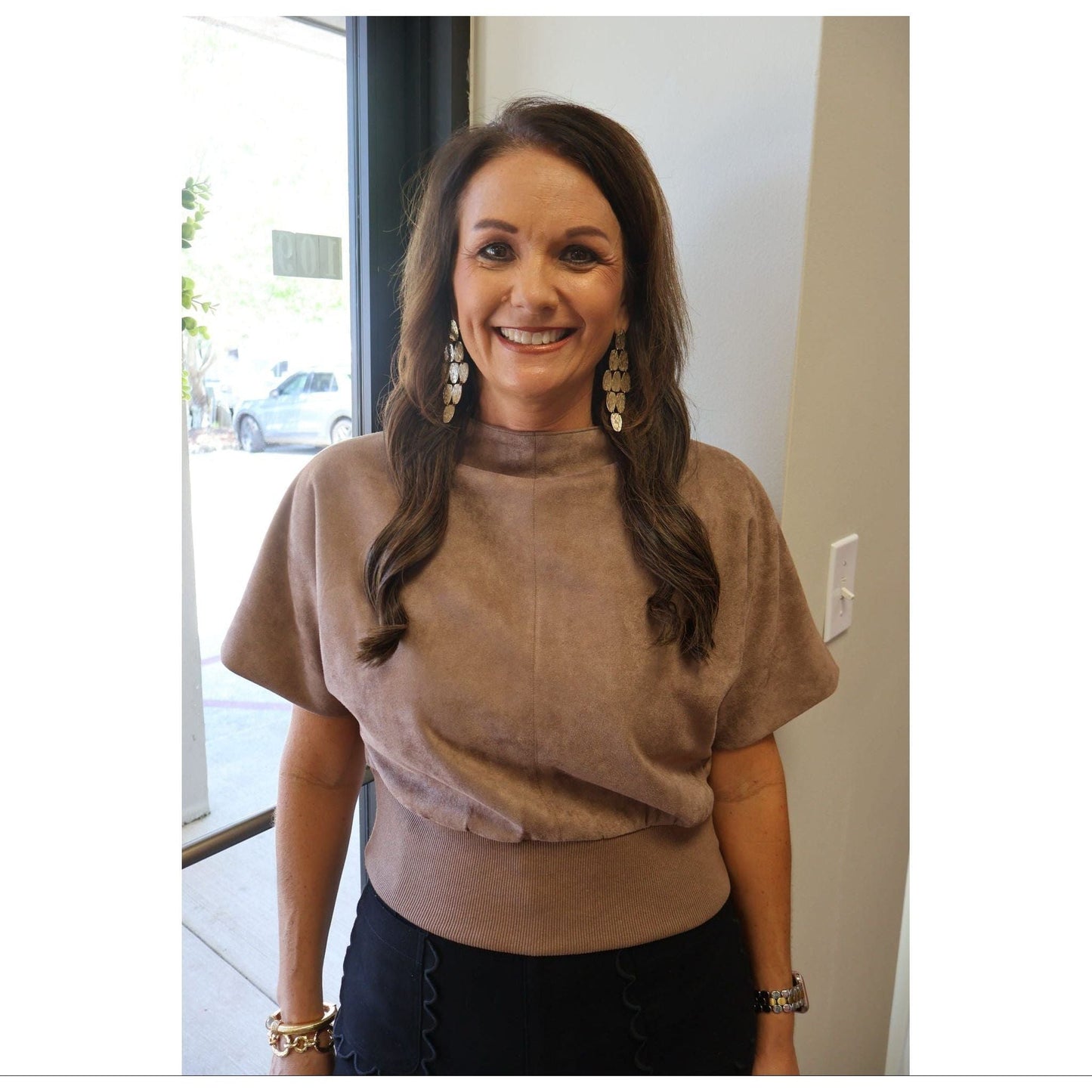 Annie Ks Boutique mocha suede-look mock neck top with short sleeves worn by a smiling woman with long brown hair.