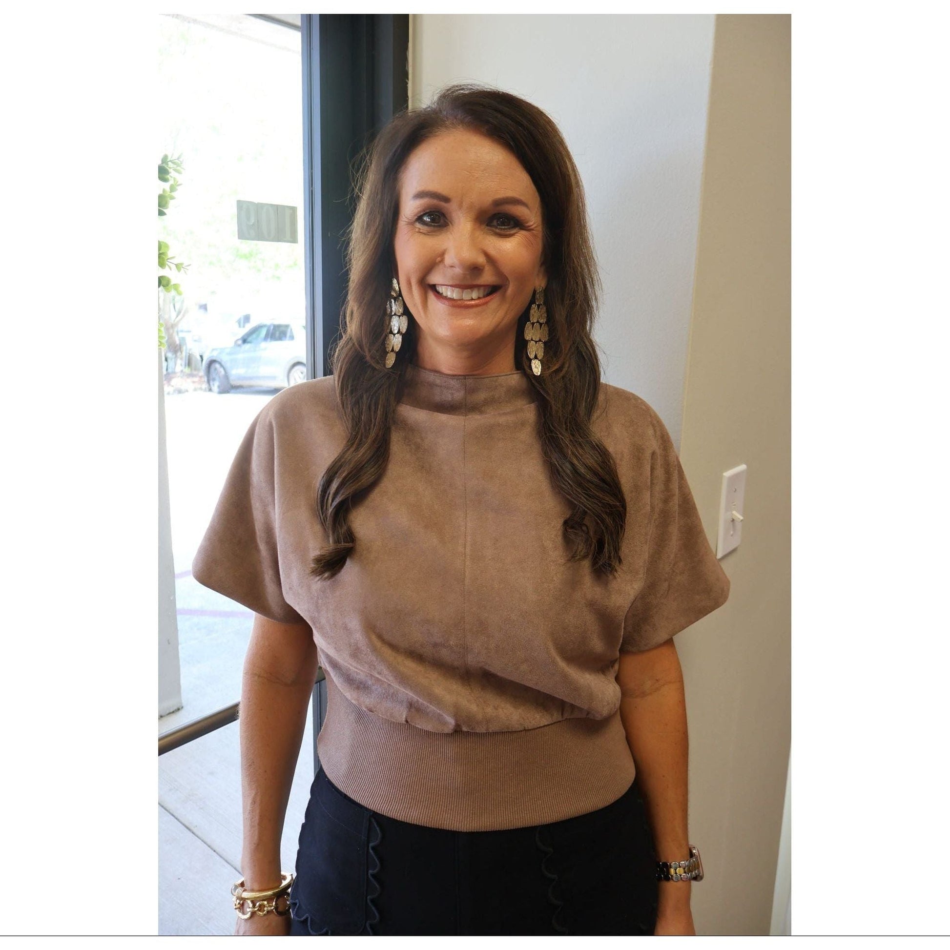 Annie Ks Boutique mocha suede-look mock neck top with short sleeves worn by a smiling woman with long brown hair.