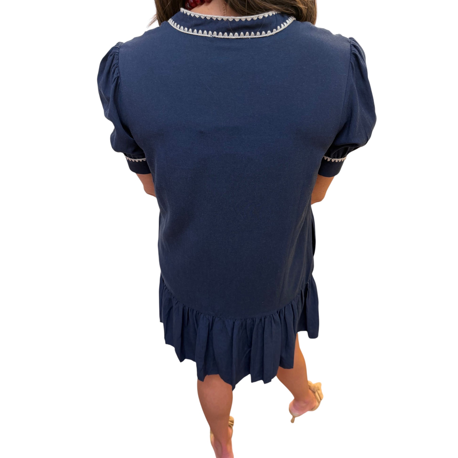 Annie Ks Boutique navy shift dress with puff sleeves, contrast embroidery trim, and a ruffled hem, back view.