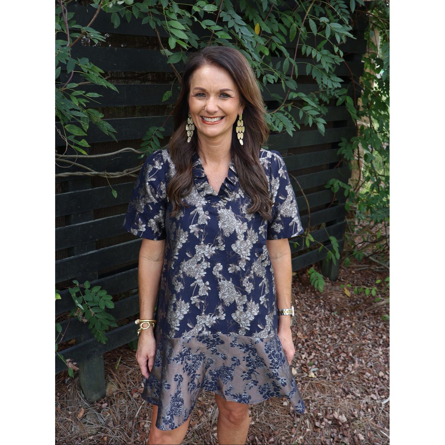 Annie Ks Boutique navy floral jacquard dress with a ruffle V-neck, drop waist, and flounce hem on a smiling model.