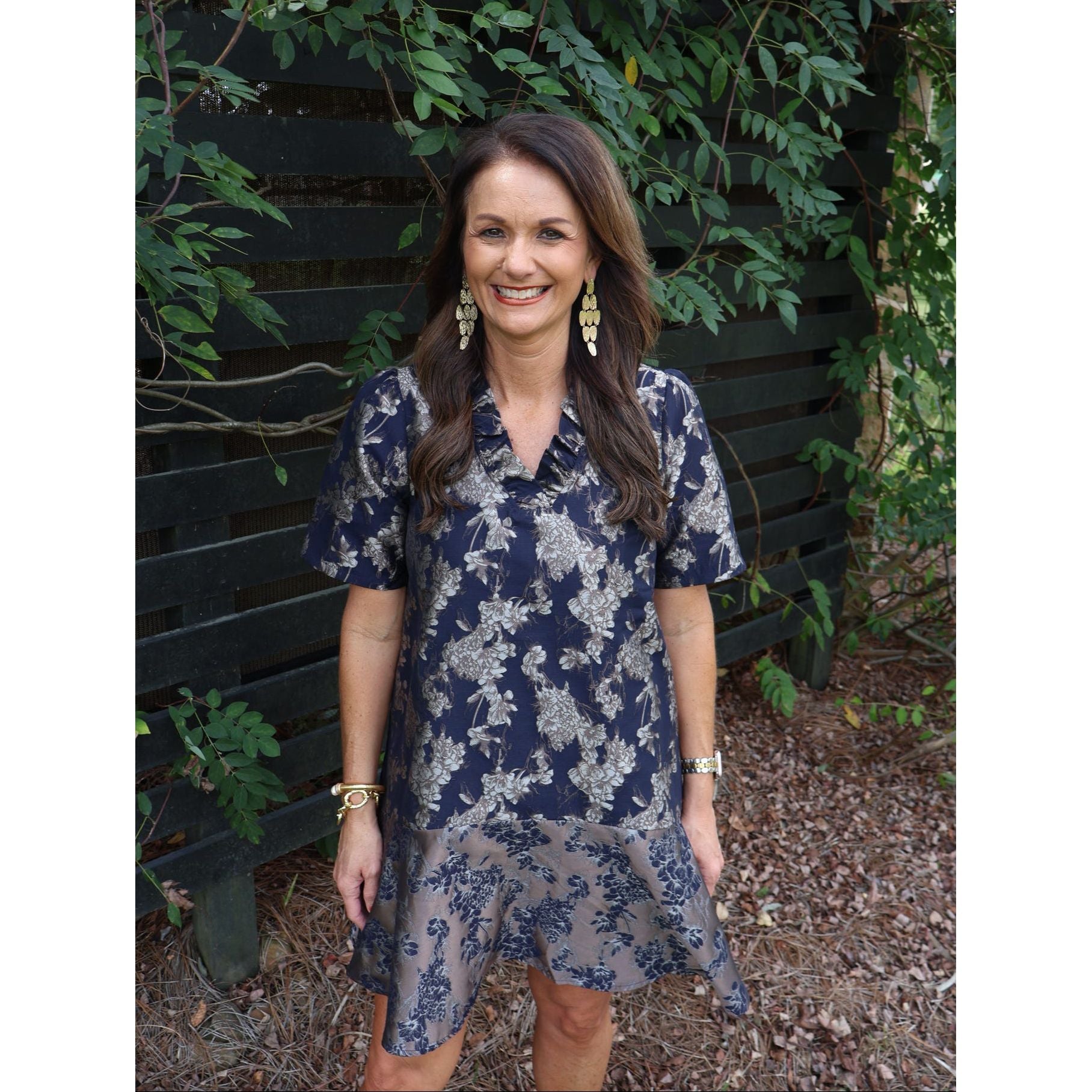 Annie Ks Boutique navy floral jacquard dress with a ruffle V-neck, drop waist, and flounce hem on a smiling model.
