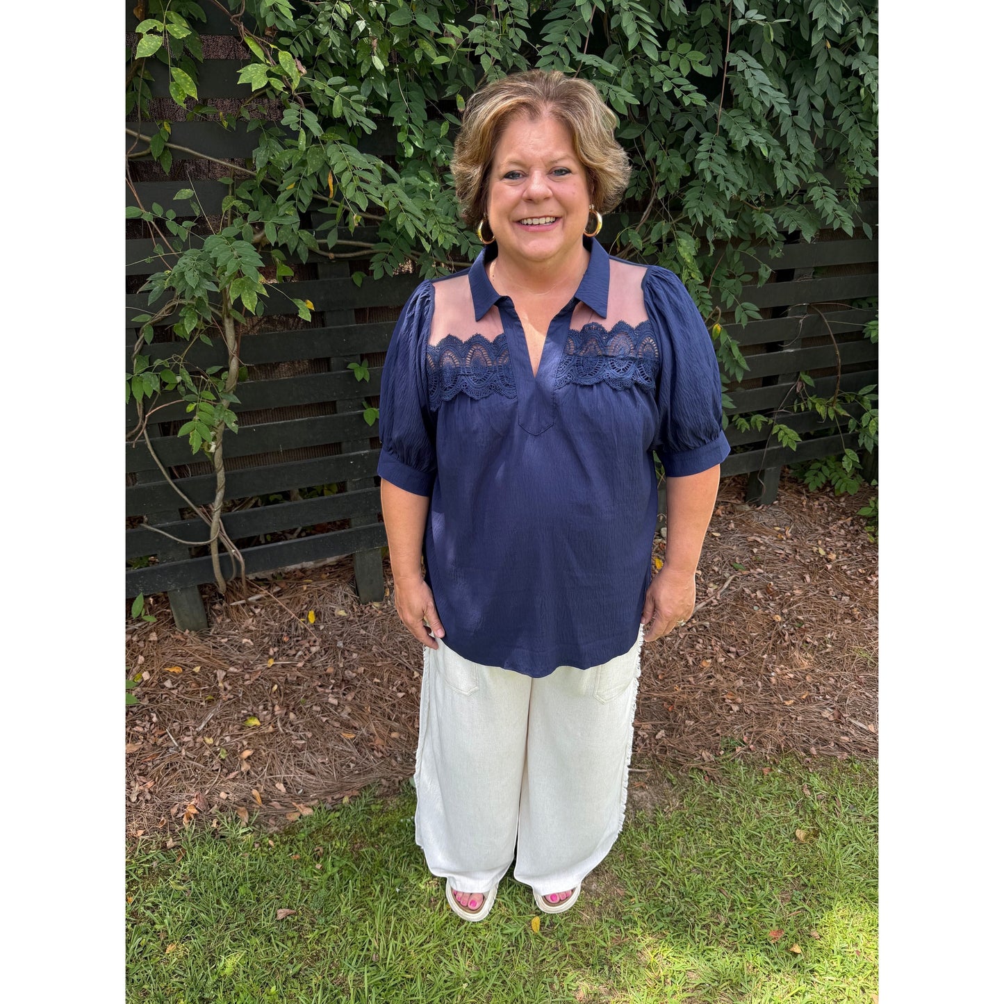 Annie Ks Boutique navy blouse with puff sleeves, lace trim, and sheer mesh shoulders worn with white wide-leg pants.