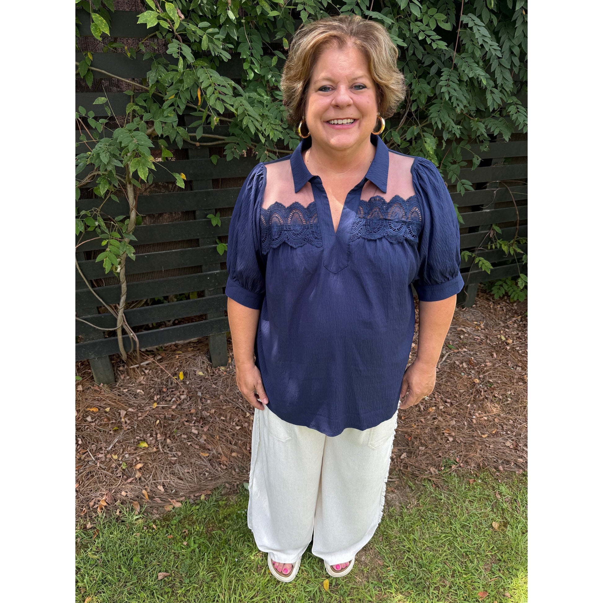 Annie Ks Boutique navy blouse with puff sleeves, lace trim, and sheer mesh panels worn with white wide-leg trousers.