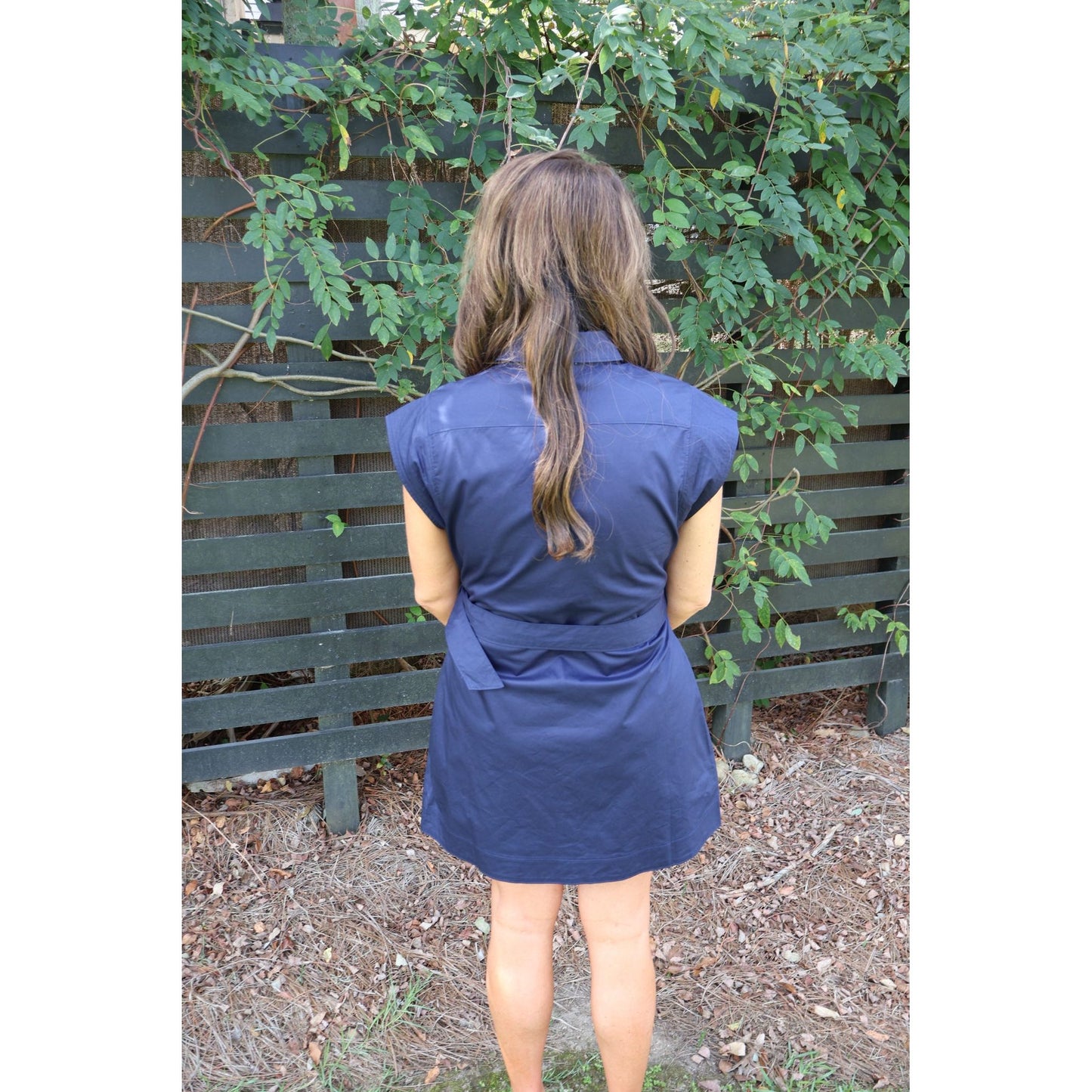 Back view of a woman wearing a navy blue sleeveless mini dress from Annie Ks Boutique with a belted waist
