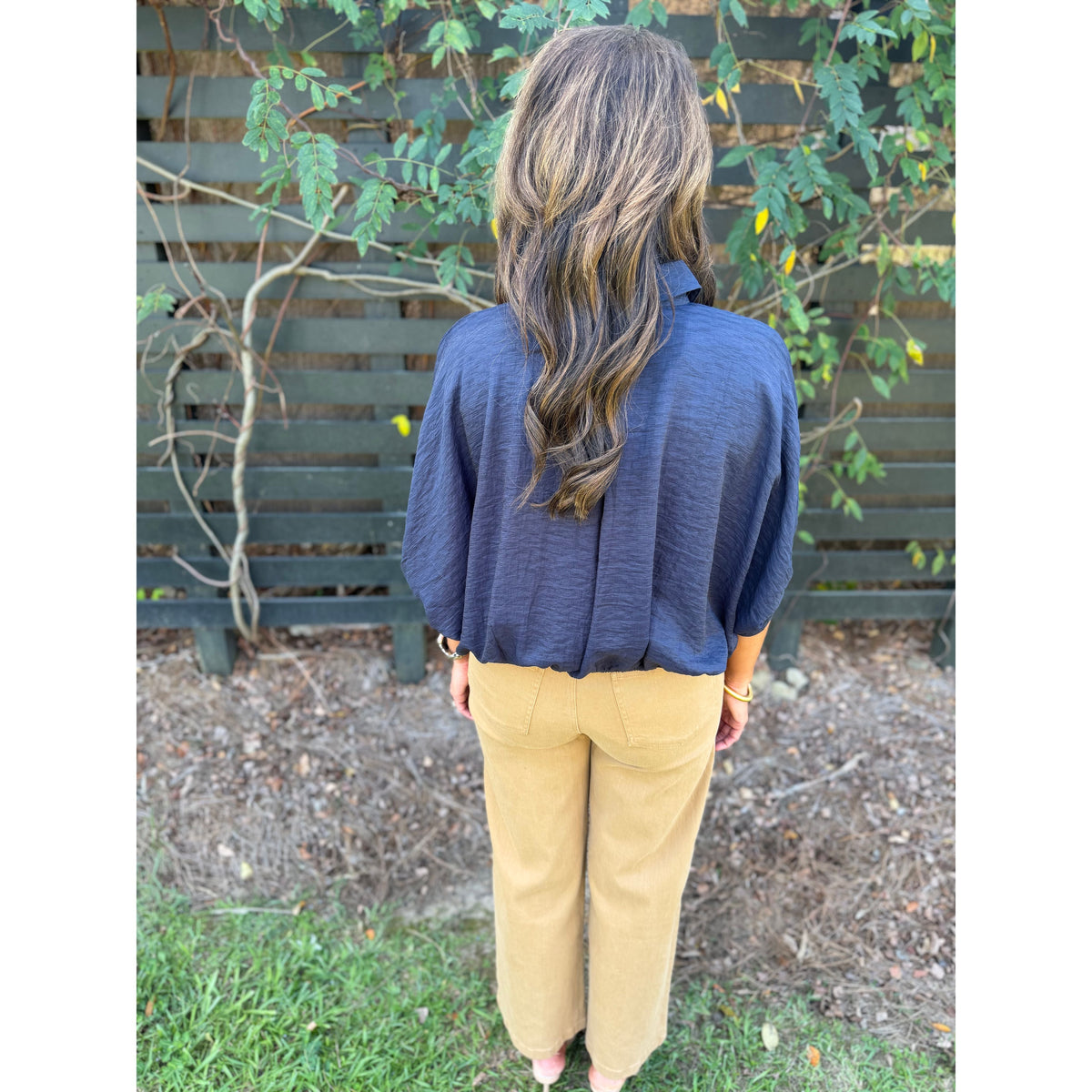 Back view of Annie Ks Boutique navy textured short sleeve blouse with dolman sleeves paired with tan trousers