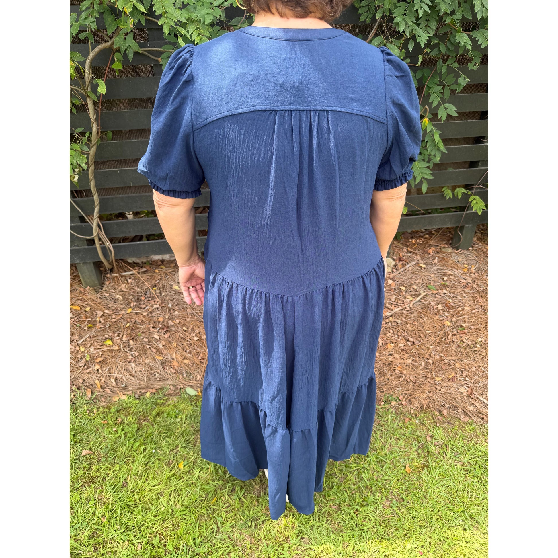 Back view of Annie Ks Boutique navy midi dress with tiered skirt and 3/4 puff sleeves in a garden setting