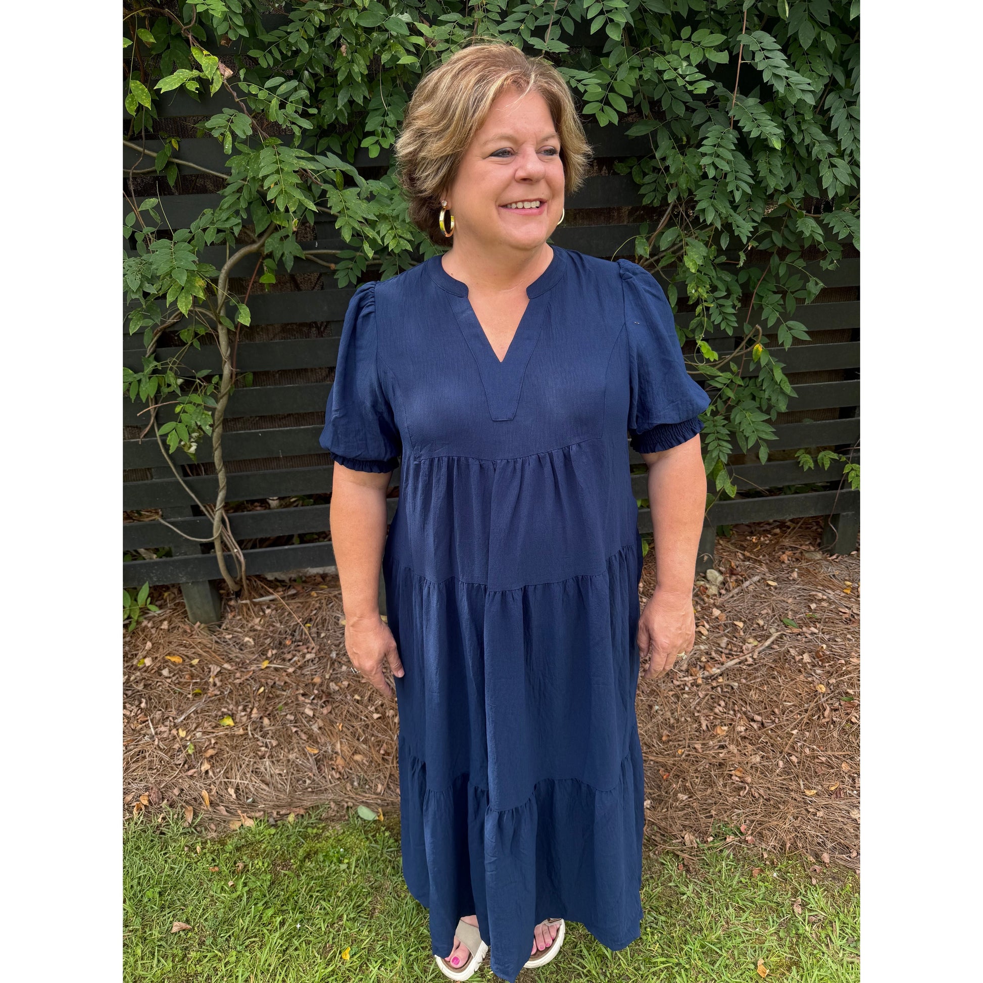 Woman wearing an Annie Ks Boutique navy blue tiered midi dress with V-neckline and 3/4 puff sleeves in a garden.