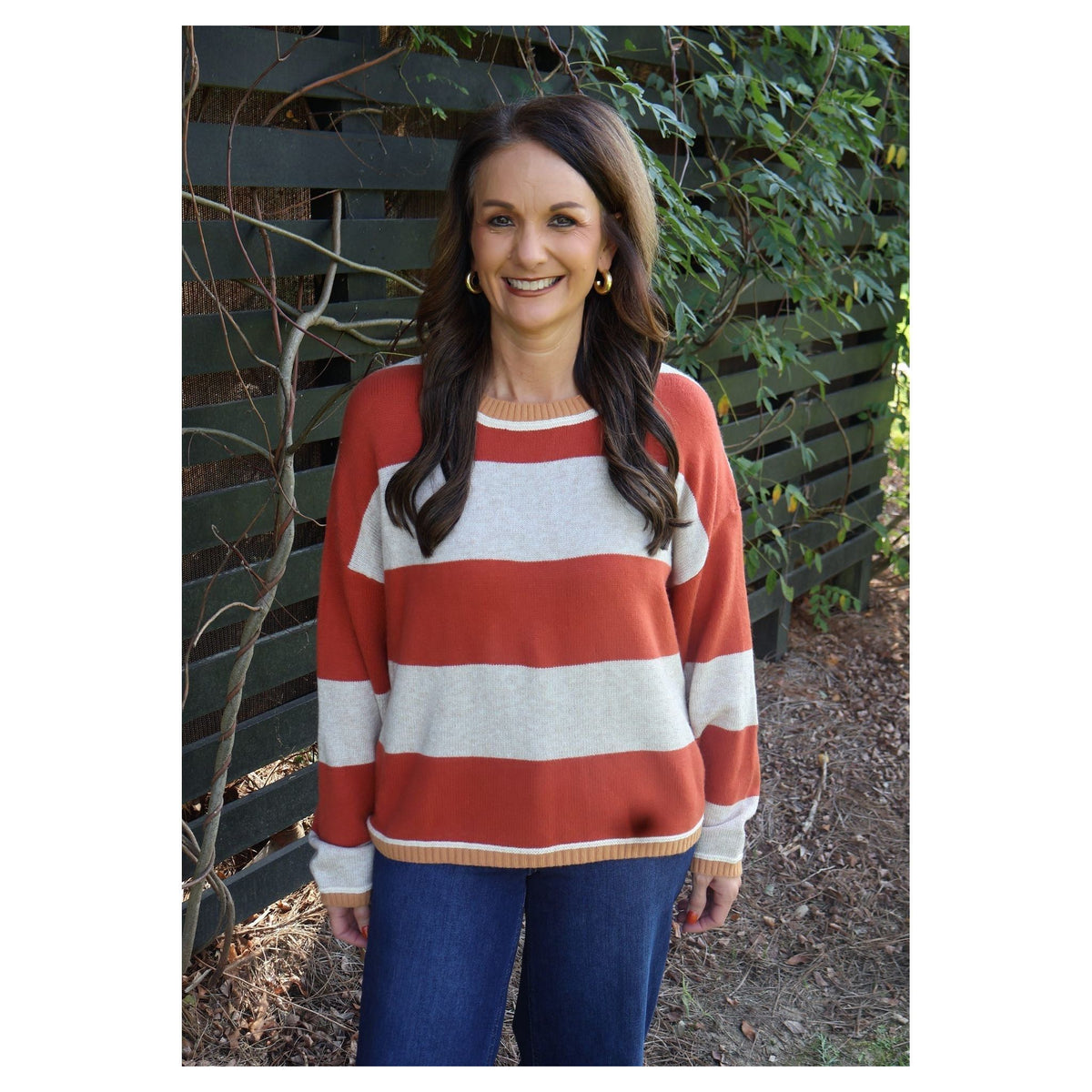 Annie Ks Boutique model wearing an oatmeal and brick red wide-striped cozy knit sweater with a crew neckline.