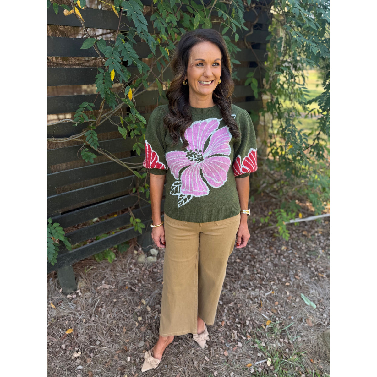 Annie Ks Boutique olive sweater with pink floral print and puff sleeves worn with tan trousers in an outdoor setting.