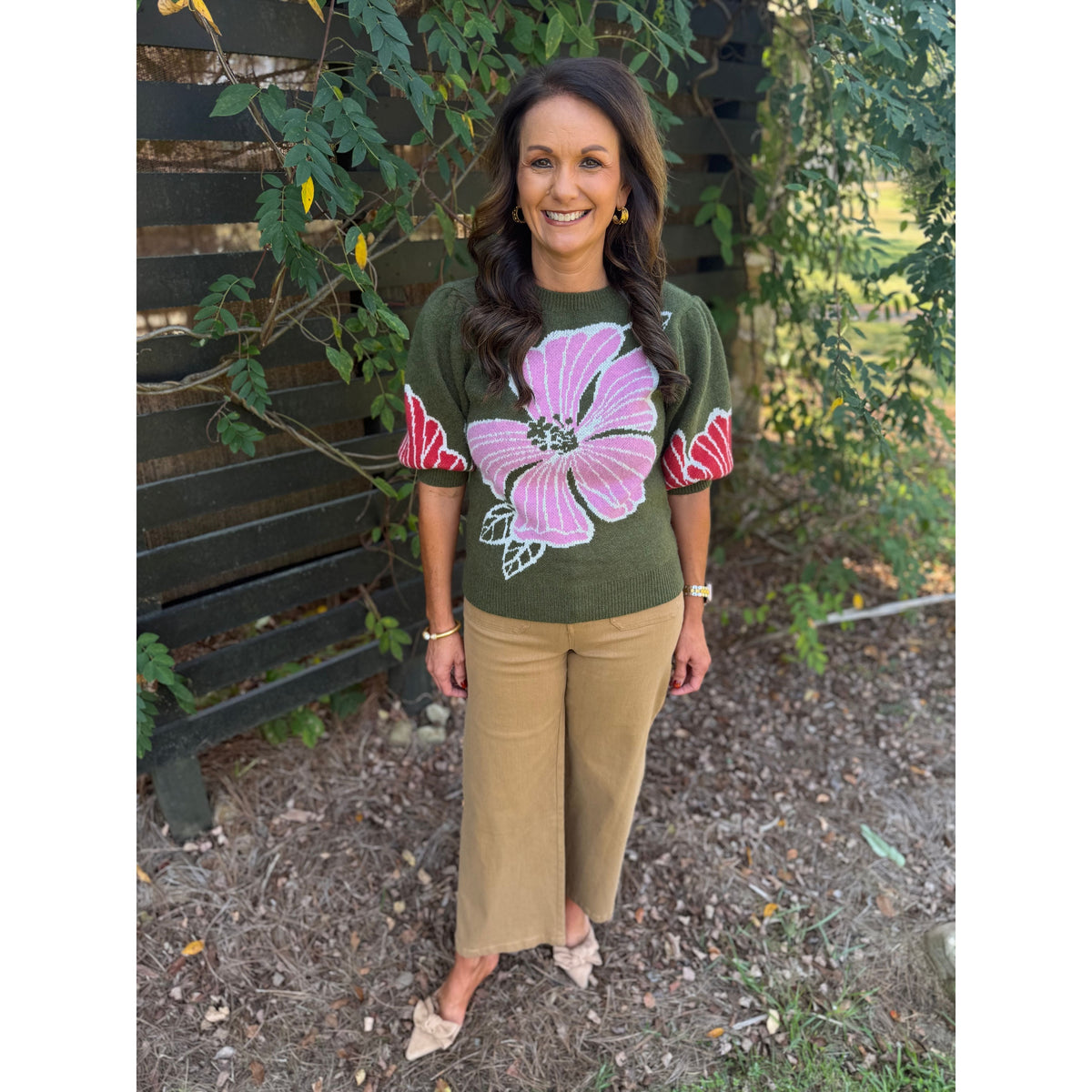 Annie Ks Boutique olive sweater with pink floral print and puff sleeves worn with tan trousers by a smiling woman