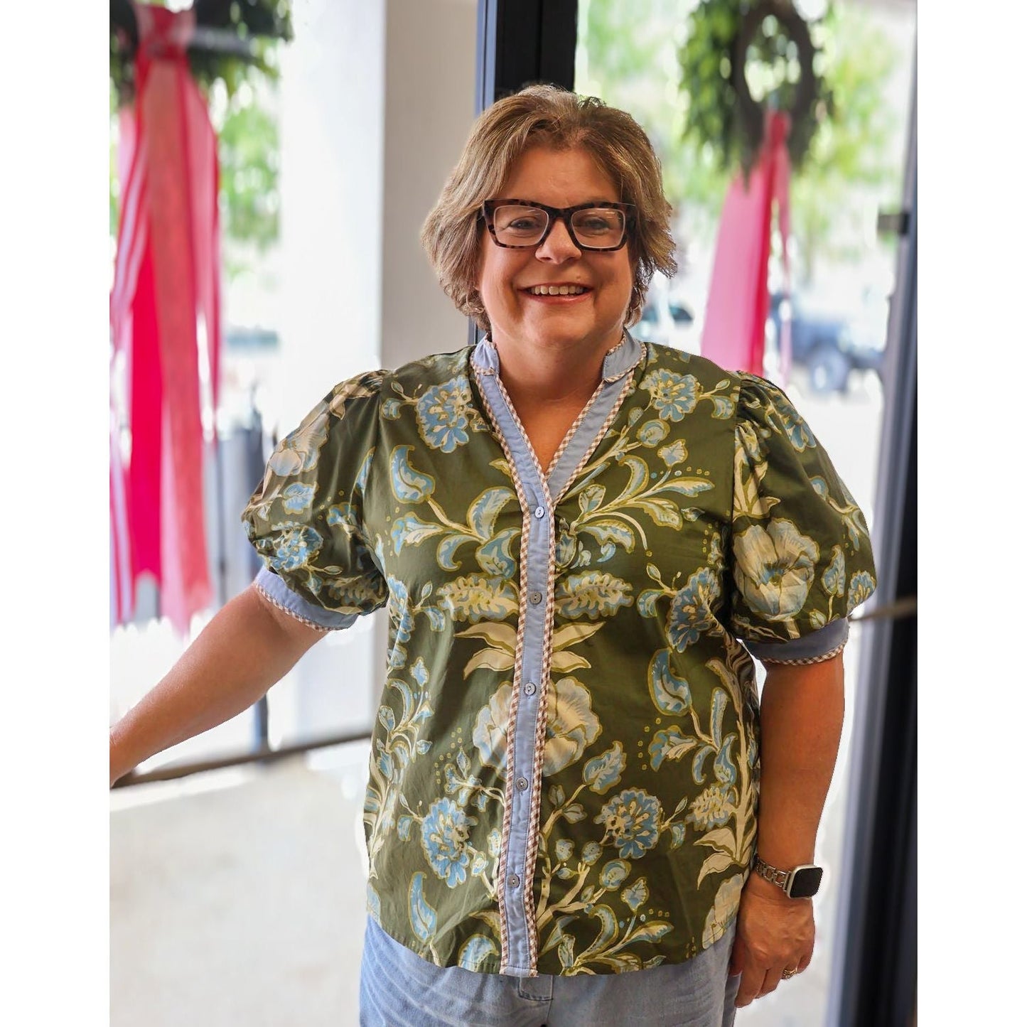 Annie Ks Boutique curvy olive floral puff sleeve cotton top with button front and contrast trim on a smiling woman.
