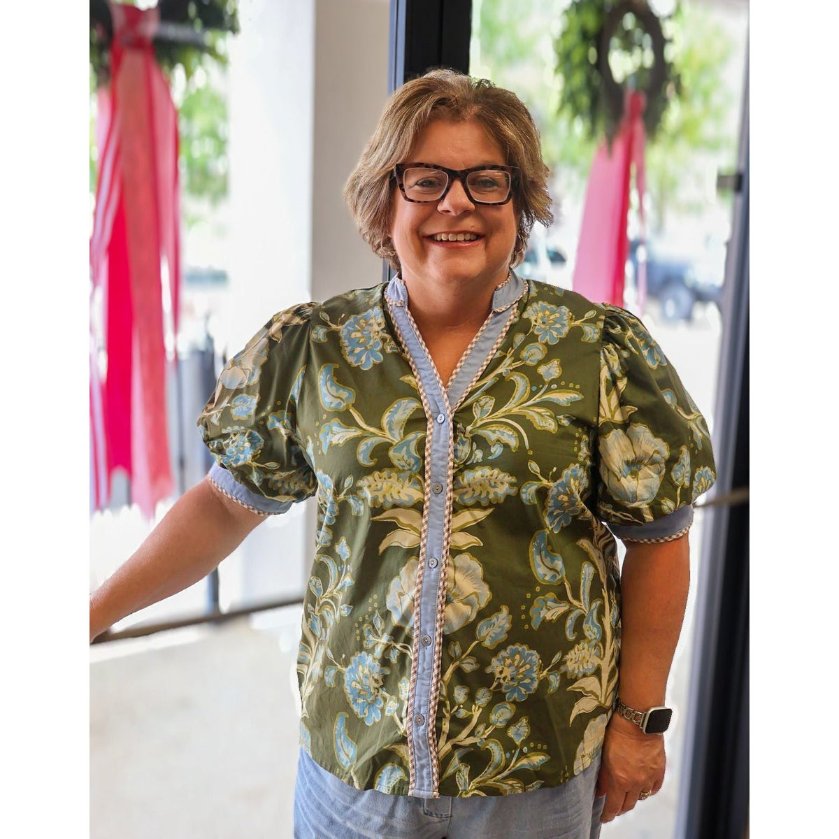 Annie Ks Boutique curvy olive floral puff sleeve cotton top with button front and contrast trim on a smiling woman.