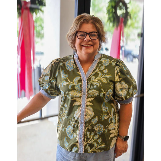 Annie Ks Boutique curvy olive floral puff sleeve cotton top with button front and contrast trim on a smiling woman.