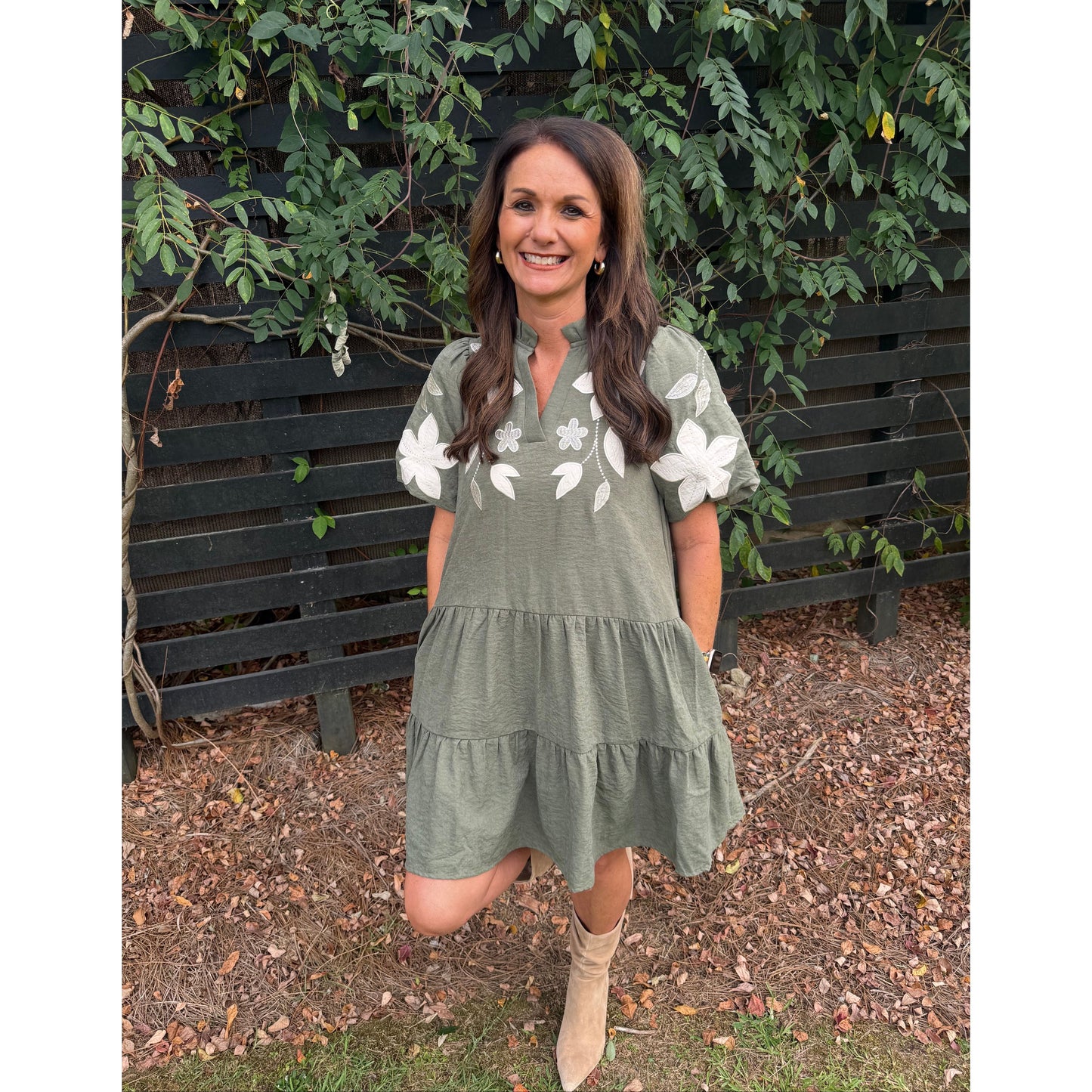 Annie Ks Boutique olive tiered mini dress with white floral applique, split neckline, and puff sleeves on a woman.