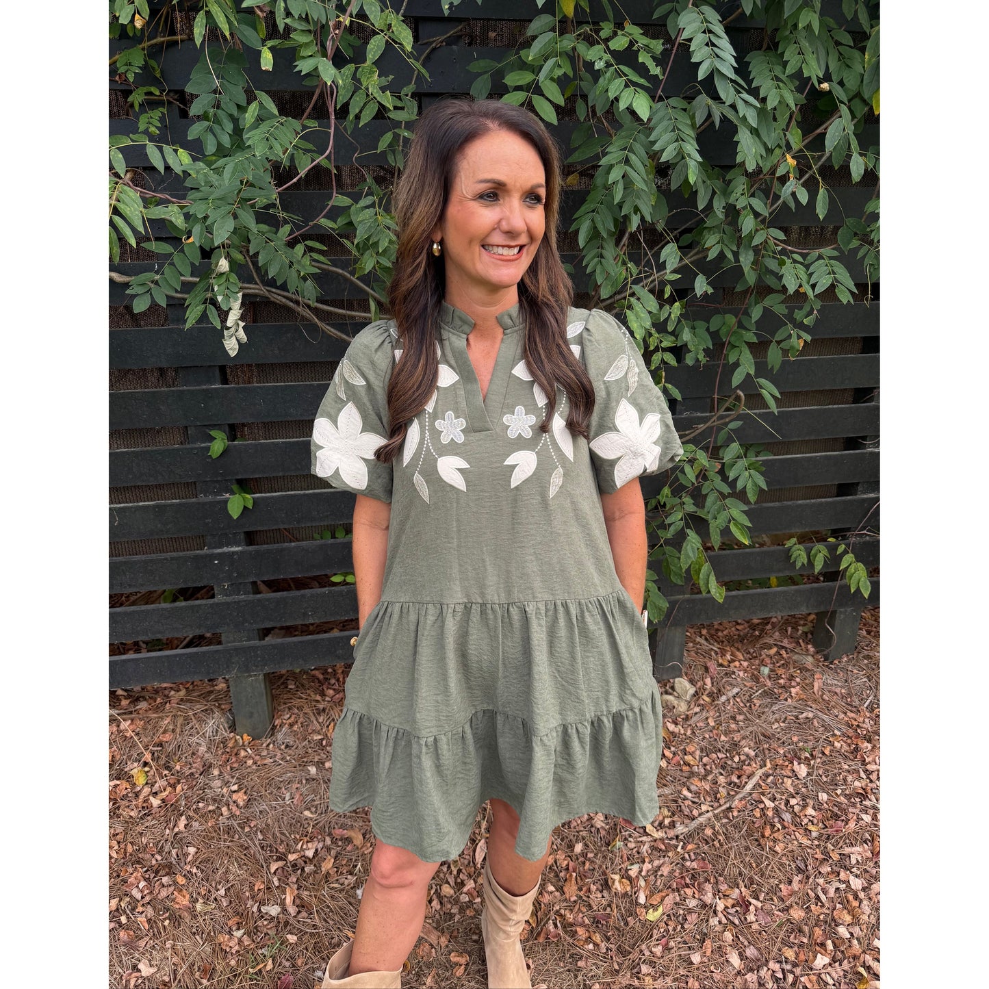 Annie Ks Boutique olive tiered mini dress with white floral applique, split neckline, and puff sleeves on a woman