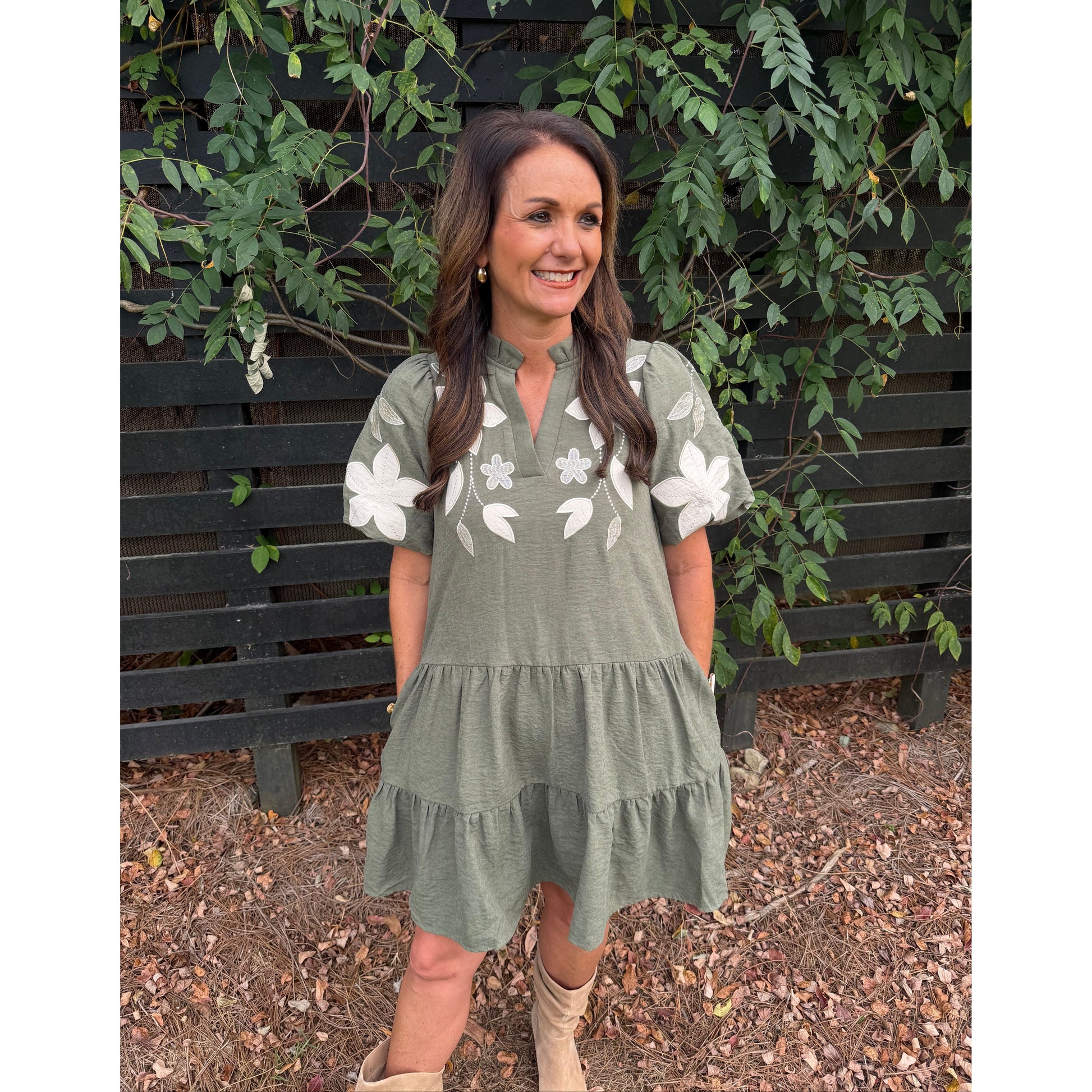 Annie Ks Boutique olive tiered mini dress with white floral applique, split neckline, and puff sleeves on a woman