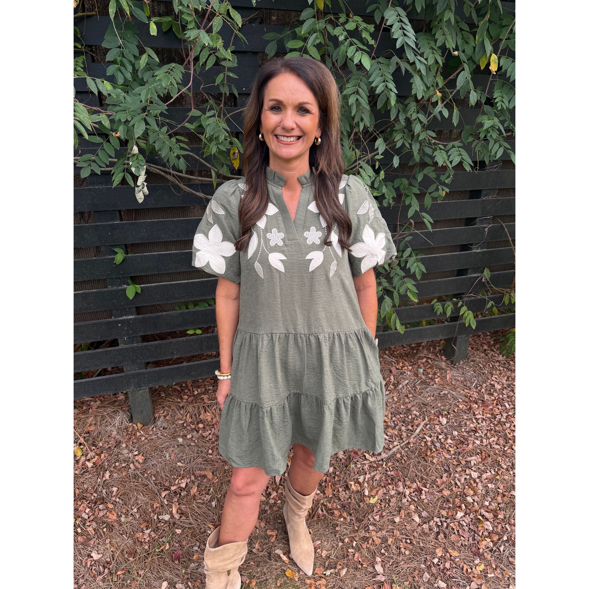 Annie Ks Boutique olive tiered mini dress with white floral applique, split neckline, and puff sleeves on a woman.