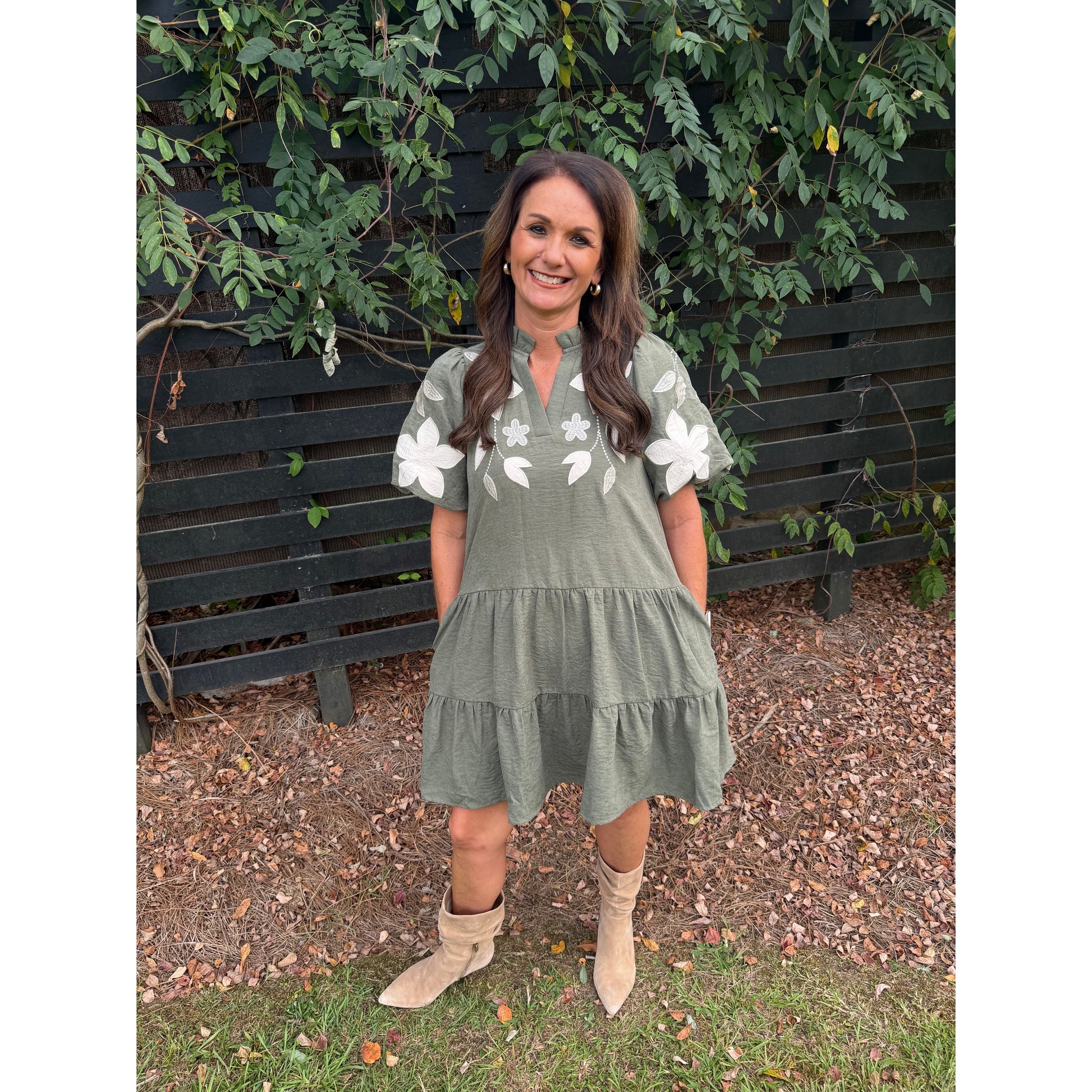 Annie Ks Boutique olive tiered mini dress with white floral applique, puff sleeves, and split neckline on a woman.