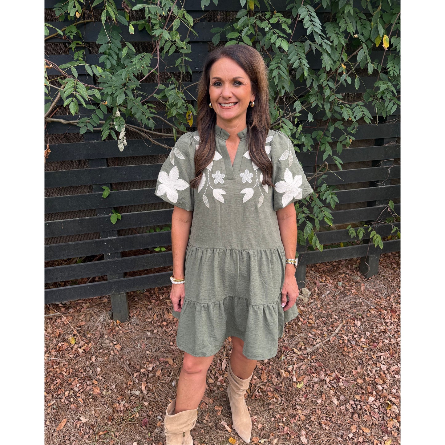 Annie Ks Boutique olive tiered mini dress with white floral applique, split neckline, and puff sleeves on a woman.