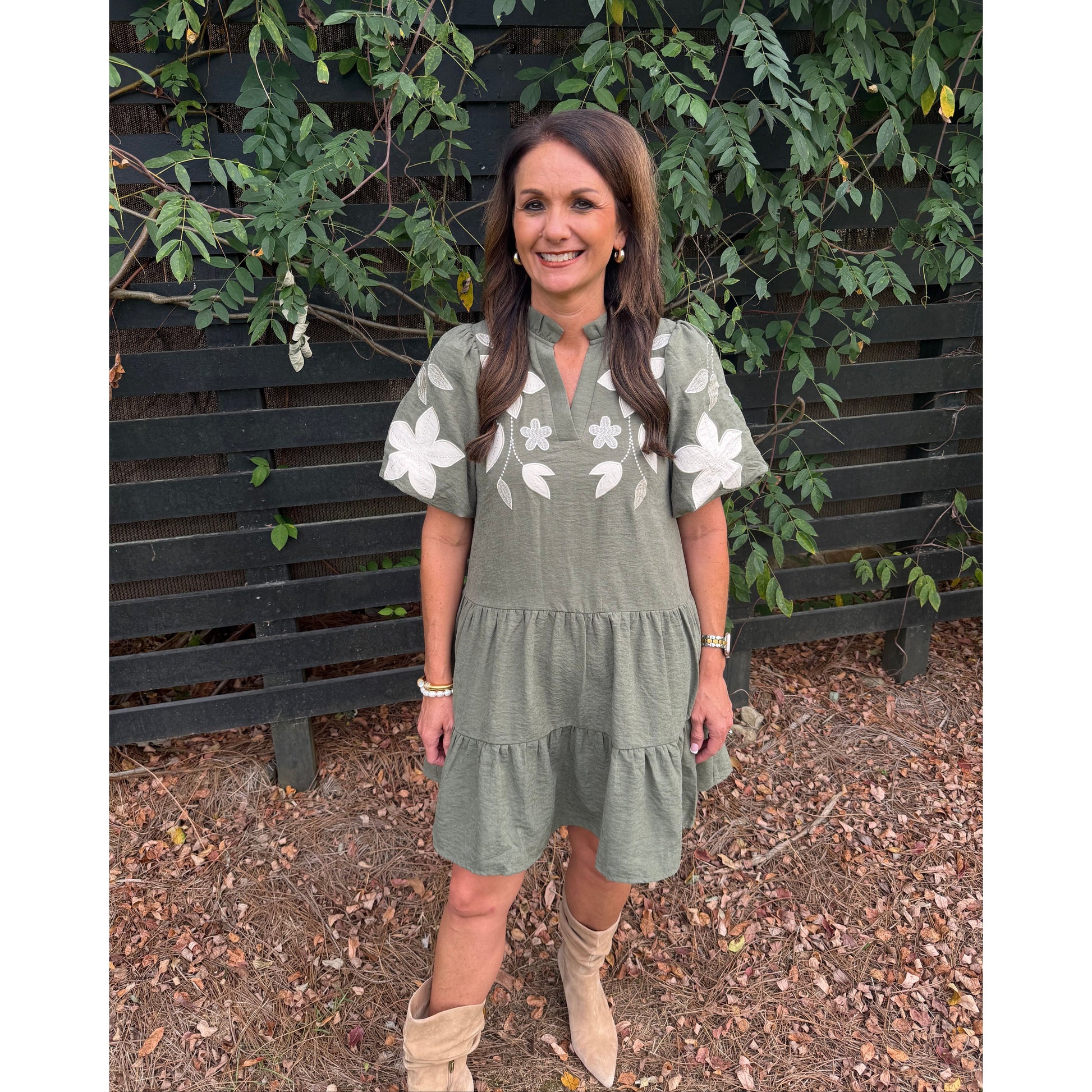 Annie Ks Boutique olive tiered mini dress with white floral applique, split neckline, and puff sleeves on a woman.