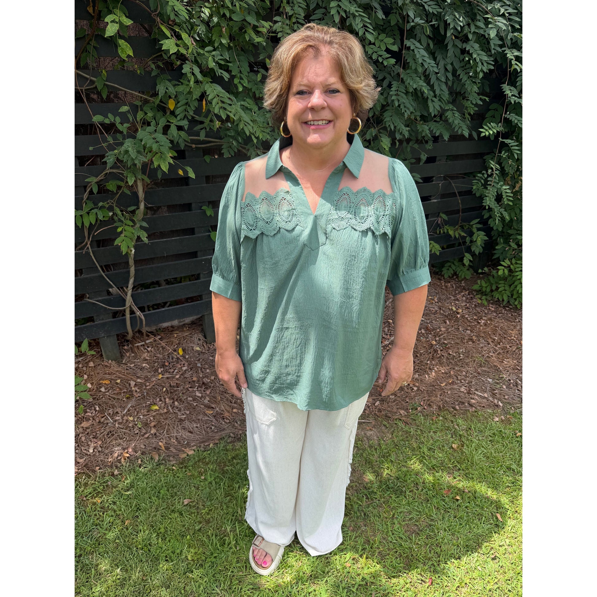 Annie Ks Boutique olive blouse with puff sleeves, lace trim, and sheer mesh panels worn by a smiling woman outdoors.