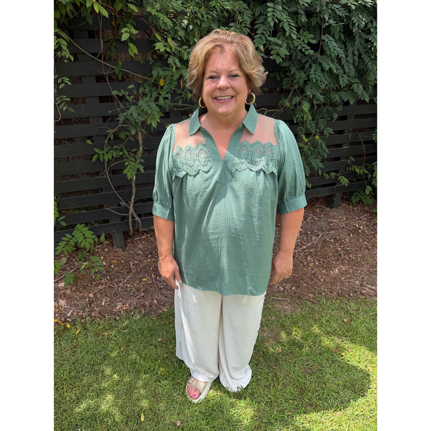 Annie Ks Boutique olive blouse with puff sleeves, lace trim, and sheer mesh panels worn by a smiling woman outdoors.
