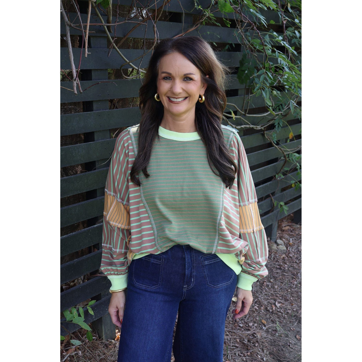 Annie Ks Boutique model wearing a loose fit olive and latte mixed stripe top with dark wash wide leg jeans