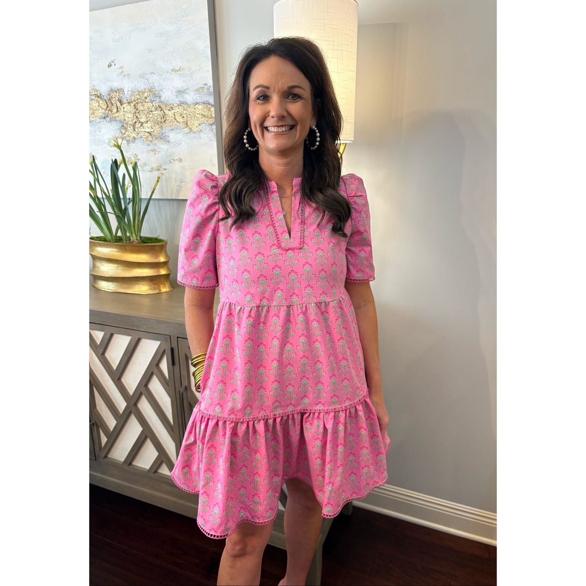 A woman wearing an Annie Ks Boutique pink mini dress with puff sleeves, scallop trim, and a split V-neckline.