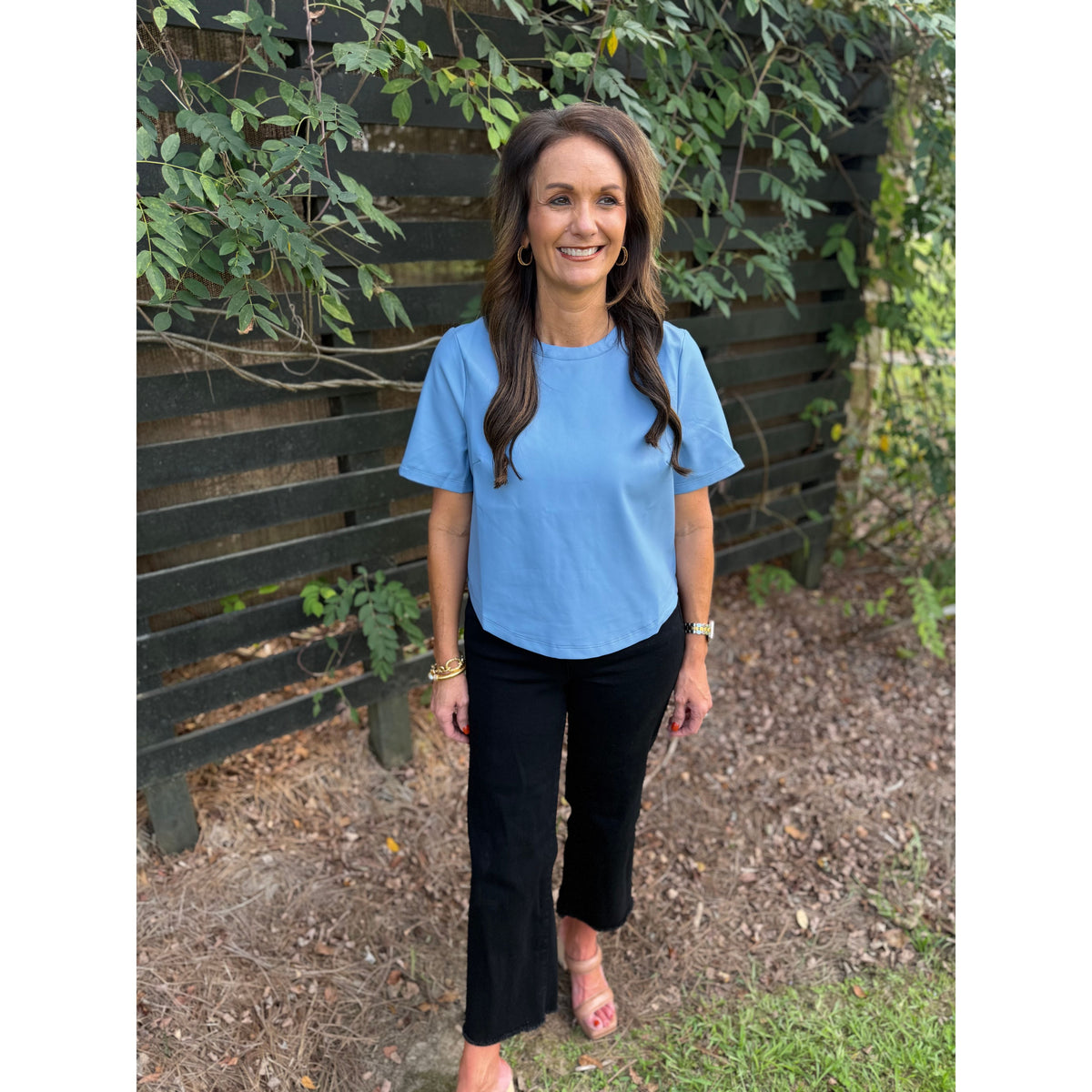Annie Ks Boutique powder blue faux leather short-sleeve top worn by a woman with black trousers in an outdoor setting.