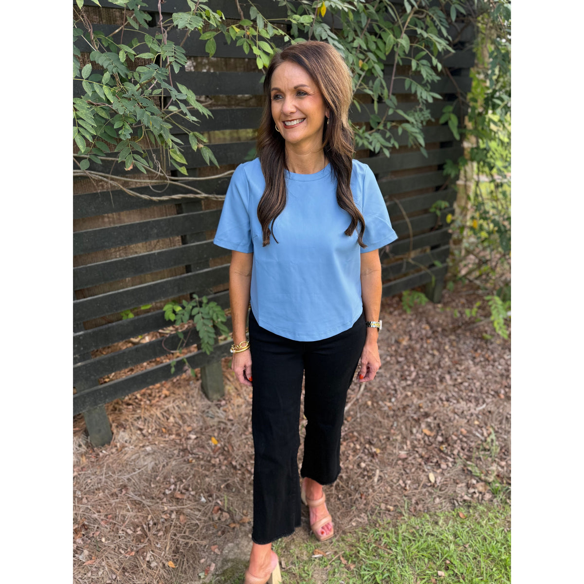 Annie Ks Boutique powder blue faux leather short-sleeve top worn by a woman with black trousers in a garden setting