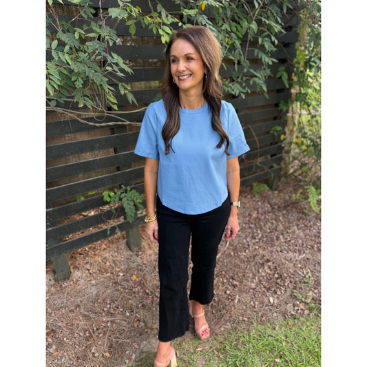 Annie Ks Boutique powder blue faux leather short-sleeve top worn by a woman with black trousers in a garden setting