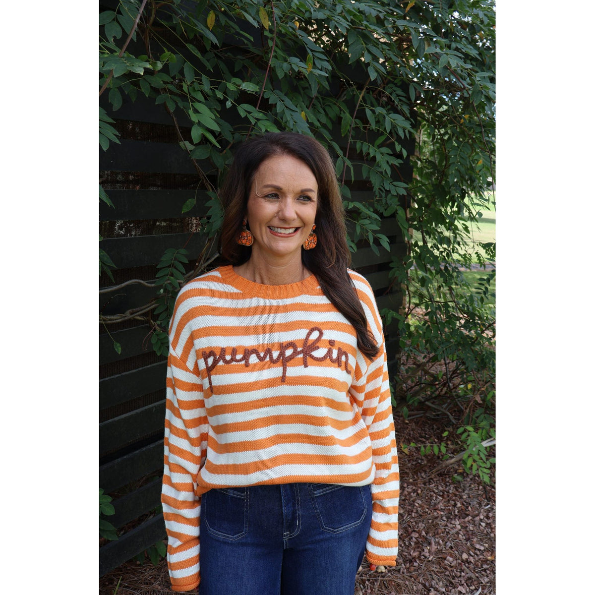Annie Ks Boutique model wearing an orange and ivory striped knit sweater with pumpkin script and ribbed trim.