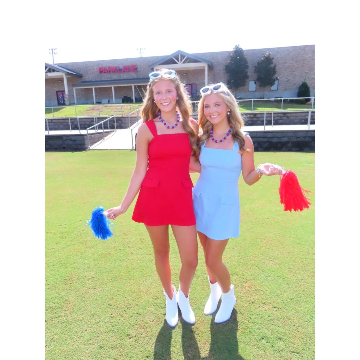 Two women wearing Annie Ks Boutique red and light blue mini skort rompers with white boots on a sunny field