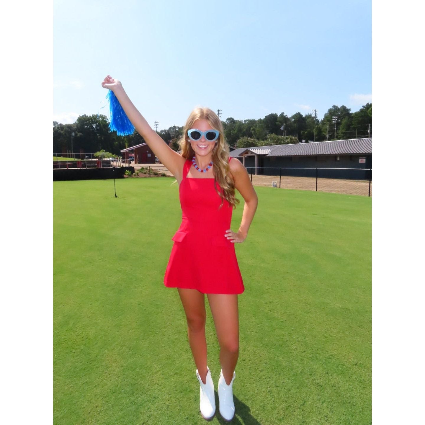 Annie Ks Boutique red mini skort romper with straight neckline and faux pockets worn by a woman with blue pom-poms.