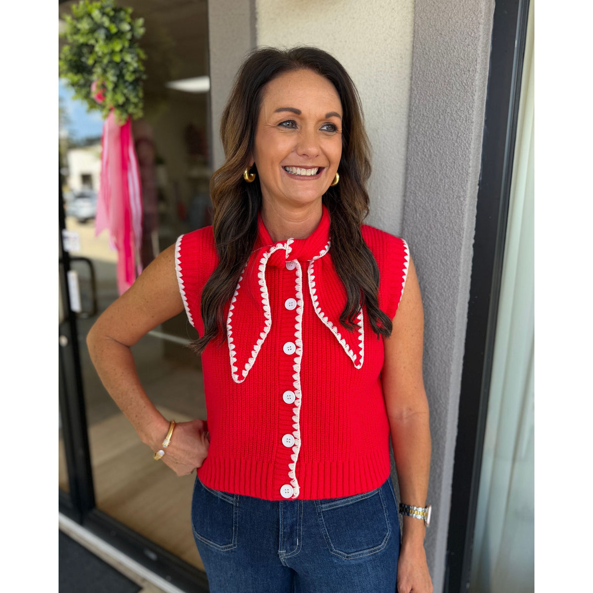Annie Ks Boutique red sweater vest with white contrast stitching, button-down front, and tie neck worn by a woman.