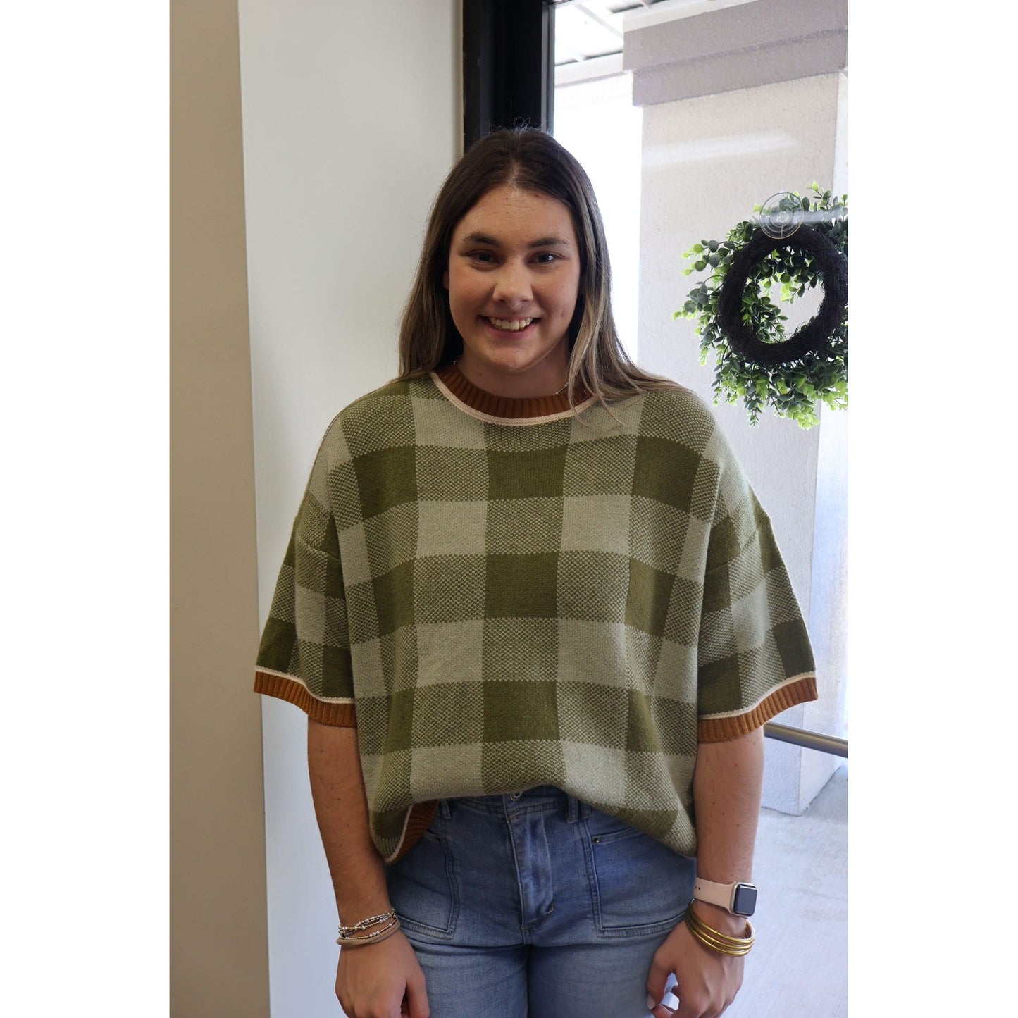 Annie Ks Boutique sage and olive checkered drop shoulder sweater top worn by a smiling woman with blue jeans