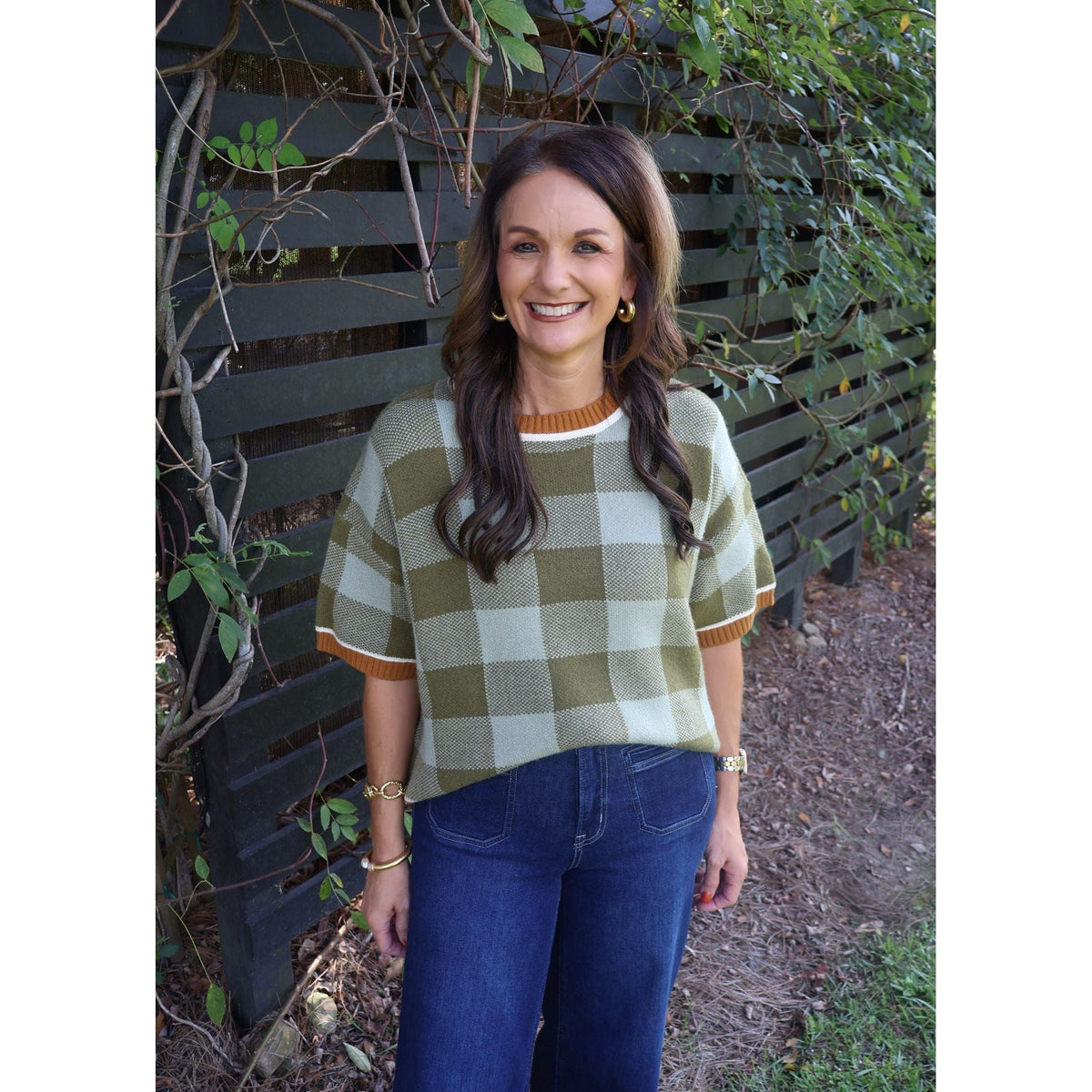 Annie Ks Boutique model wearing a sage and olive checkered plush knit sweater with drop shoulders and dark blue jeans.