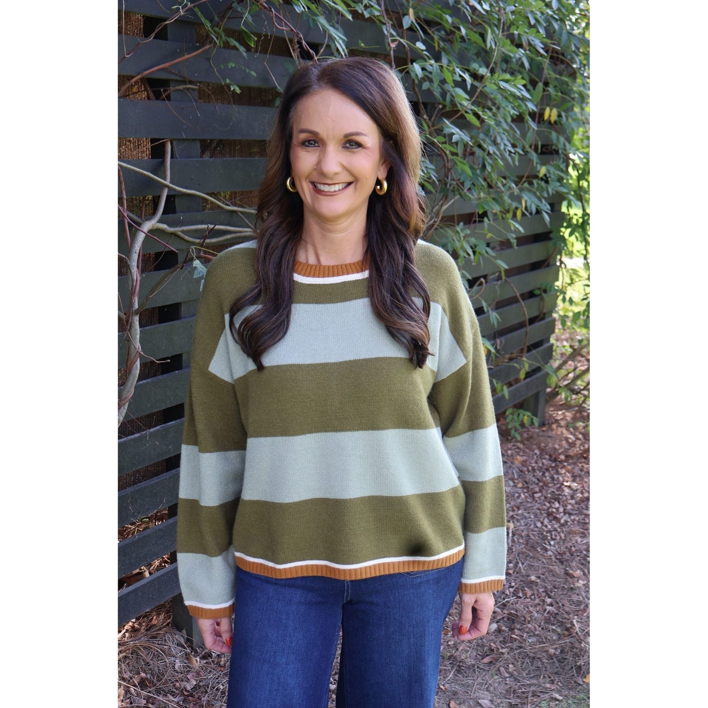Annie Ks Boutique model wearing a sage and olive green striped cozy knit sweater with a crew neck and ribbed trim.